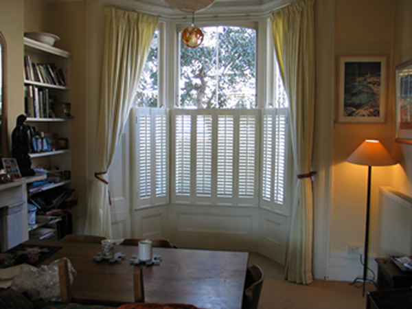 Simple lined linen curtains on bay window track with cafe shutters for privacy