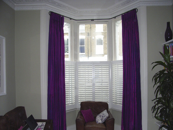 Silk curtains interlined and pinch pleated on bay window pole with cafe height shutters for privacy